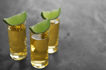 Gold tequila shots with lime on gray table