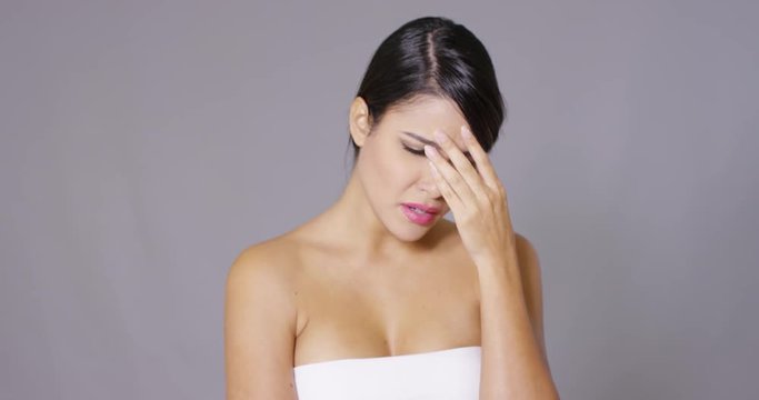 Tearful young woman with a sad expression reaching for a tissue from a box to dry her eyes  head and shoulders on grey