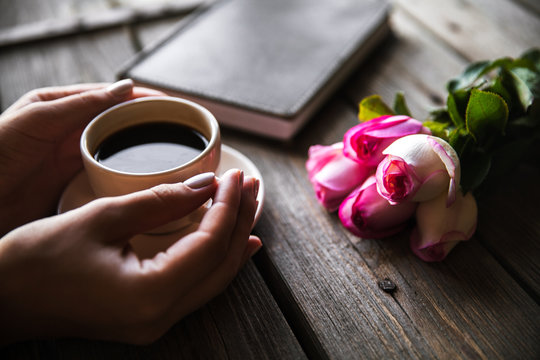 Female hand with a cup of coffee, book and flowers on wooden background. Flowers, break, work