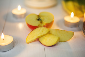 Половина яблока, дольки яблока и свечи на белом деревянном столе. 