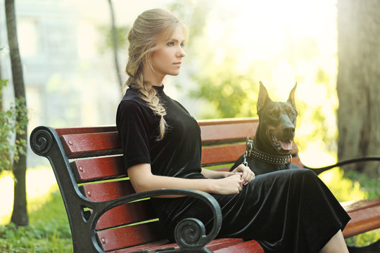 Young woman and her dog resting on wooden bench in park