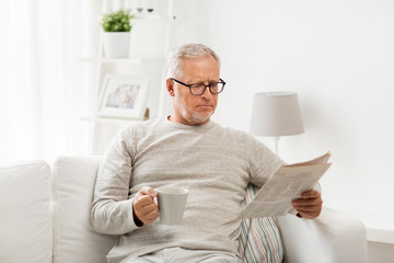 senior man in glasses reading newspaper at home