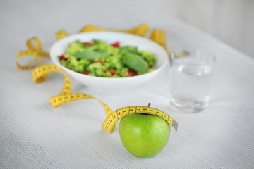 Measuring tape with green apple and vegetable salad on table