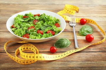 Fresh salad and measuring tape on wooden  background