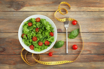Fresh salad and measuring tape on wooden  background