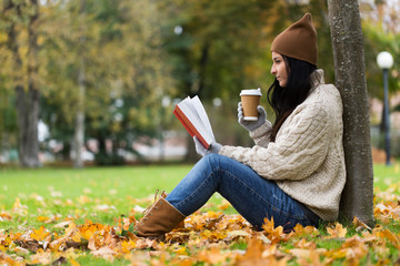 woman with book drinking coffee in autumn park