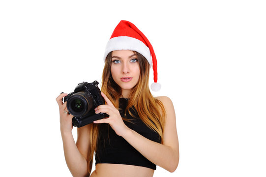 attractive young girl with the camera in a red Christmas hat on a white background. Christmas sale. Woman photographer in hat of Santa Claus. Christmas Pictures