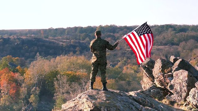 Soldier with American Flag stand  at mountain top. Slow Motion 