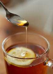 close up of woman adding honey to tea with lemon