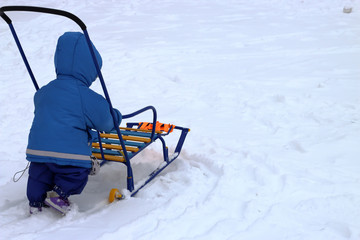 A boy makes the first steps in the winter on sleds