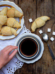 Breakfast with croissants and black coffee composition with girl hand on wooden retro background.