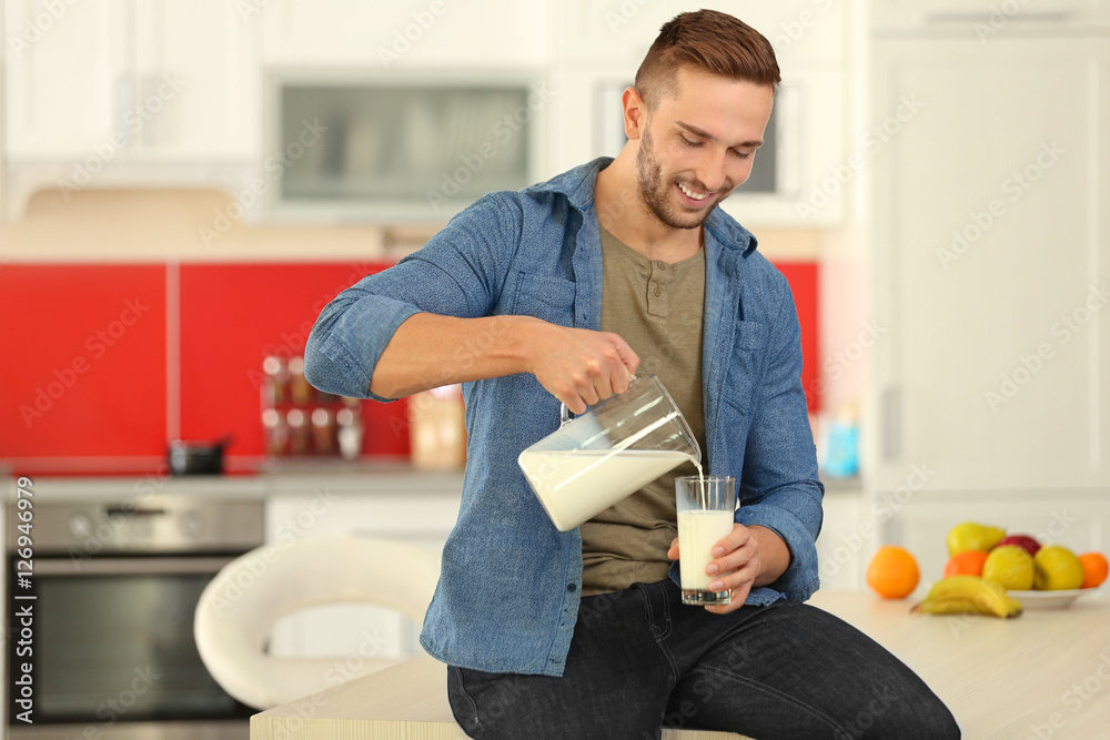 Wall mural Young man pouring fresh milk into glass at kitchen