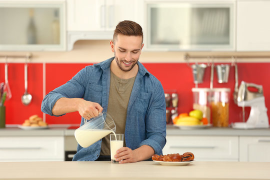 Young man pouring fresh milk into glass at kitchen