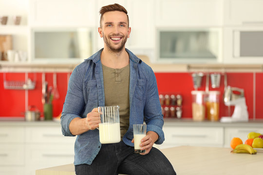 Young man with jug and glass of fresh milk at kitchen