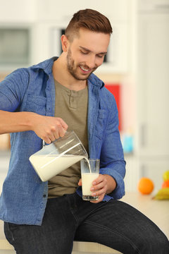 Young man pouring fresh milk into glass at kitchen
