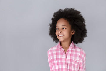 Portrait of cheerful little girl looking away and smiling while standing against grey background