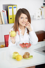 Smiling nutritionist showing apple with fresh fruit on foreground