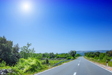 Fototapeta premium Beautiful asphalt freeway, motorway, highway without traffic through of southern landscape mountains forest during summer on a sunny day. Travel road concept.