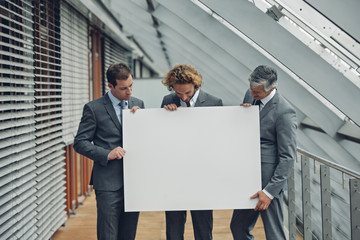 Portrait of happy business team holding a blank billboard while at office