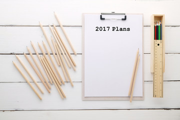 2017 plans on paper clipboard , pencils on white wood background
