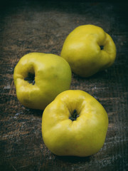 Three ripe yellow quince on a wooden background