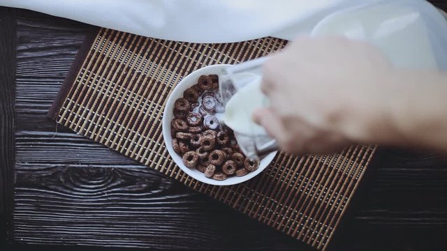 Man Pouring Milk into Krispy on a Black Wooden Table, Top view, Cereal Breakfast