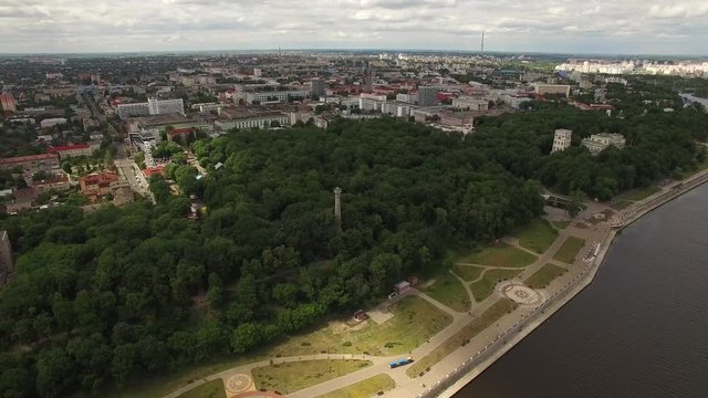 Gomel Belarus aerial 4K HD. Fly over city buildings and park at river Sozh with embankment panoramic landscape top view. Cruise motor boat move on water and green wood area bank other side by drone