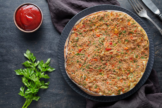 Lahmacun traditional turkish gourmet pizza with minced beef or lamb meat, paprika, tomatoes, cumin spice, parsley baked spicy middle eastern food on dark table background