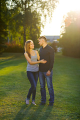 Man and woman standing on sunset light illuminated the meadow, embracing, looking at each other, full length.