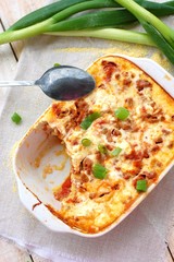 Gluten free meal roasted polenta with pork meat, spring onion, spices in white pan on grey cloth on white wooden background