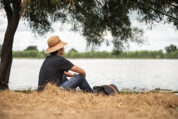 Naklejka na ściany i meble Smart man wearing hat sitting on the grass looking ahead,thinking something,the lake front.