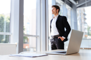 Fototapeta premium Businessman with laptop and documents standing near the window