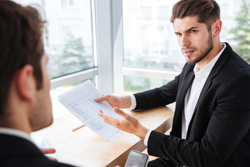 Businessman sitting and giving documents to his colleague in office