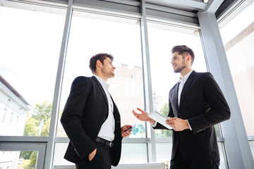 Two businessmen with tablet and mobile phone talking in office