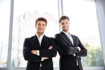 Two happy businessmen standing with arms crossed in office
