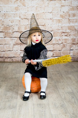 The child, a little girl in the image of the witch posing in a studio with a pumpkin and a broom on proazdnik Halloween.