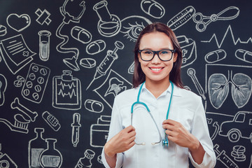 Smiling young woman doctor in glasses and white coat standing on dark background with pattern