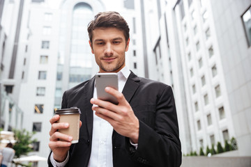 Businessman using cell phone and drinking coffee in the city