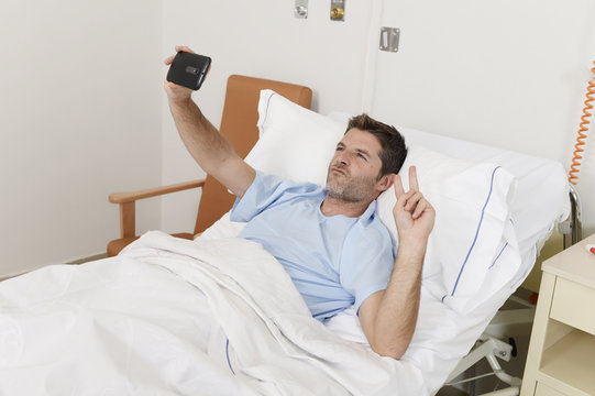 attractive man lying on bed hospital clinic holding mobile phone taking self portrait selfie photo