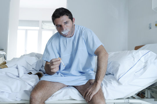 young attractive man looking sad and worried at hospital bed smoking cigarette in clinic bedroom