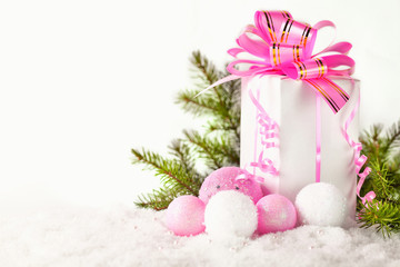 Fototapeta na wymiar White greeting card with copy space for christmas or new year with a wrapped gift, fir branches and pink ball on snow.