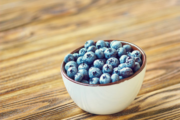 Freshly picked blueberries in white bowl. Juicy and fresh blueberries on rustic table. Bilberry on wooden Background. Blueberry antioxidant. Concept for healthy eating and nutrition.