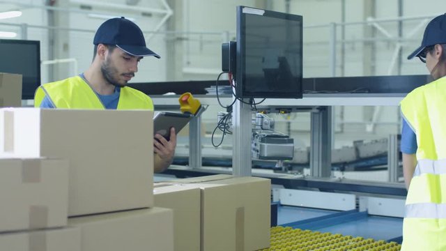 Post Sorting Center Worker Puts Cardboard Boxes on Belt Conveyor while Another Worker using Tablet PC. Shot on RED Cinema Camera in 4K (UHD)