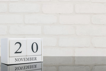 Closeup white wooden calendar with black 20 november word on black glass table and white brick wall...