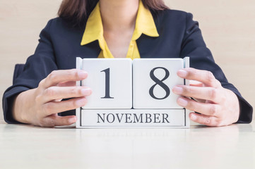 Closeup white wooden calendar with black 18 november word in blurred working woman hand on wood desk in office room , selective focus at the calendar
