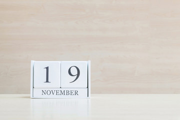 Closeup surface white wooden calendar with black 19 november word on blurred brown wood desk and wood wall textured background with copy space , selective focus at the calendar