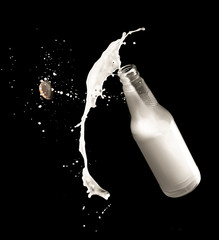 Milk bottle and splashes isolated on black background