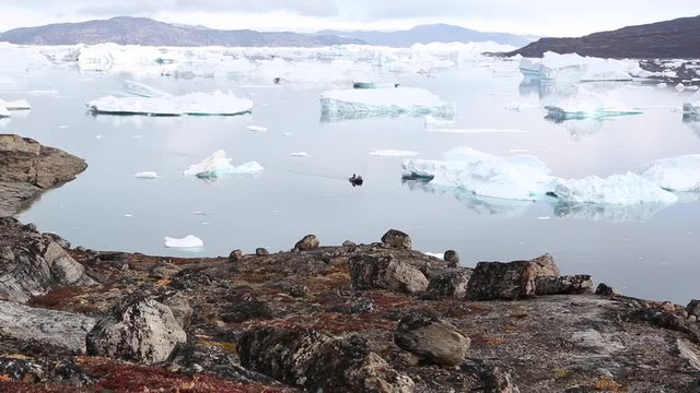 A zodiac boat trails through a fjord full of icebergs, in the background is a glacier