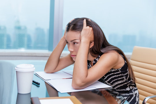 Stressed business woman at office desk stressing about work. Negative concept, headache, migraine. Tired businesswoman sitting thinking about problems and showing dissatisfaction of career.