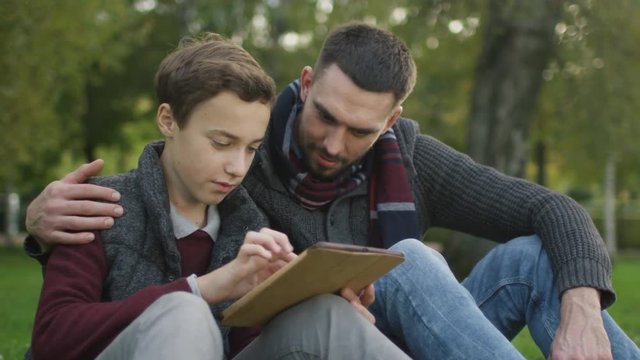 Son and Father Using Tablet Sitting in the Park